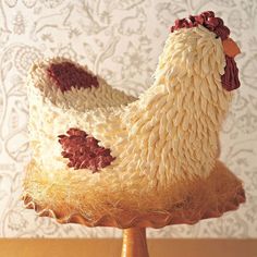 a cake made to look like a chicken sitting on top of a wooden stand in front of a wall