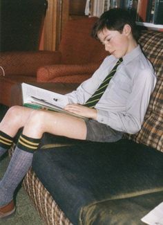 a young man sitting on top of a couch wearing a tie and reading a book