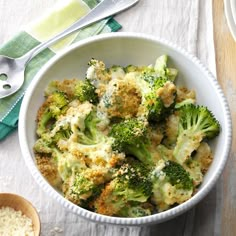 a bowl filled with broccoli and cheese next to two spoons on a table