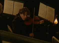 two men playing violin in the dark with sheet music on the wall behind them,