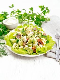 a white plate topped with lettuce salad next to a knife and fork on top of a table