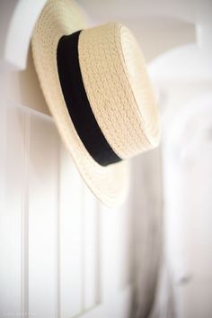 a straw hat hanging on the side of a white door with a black ribbon around it