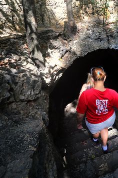 a woman in a red shirt is looking into a cave