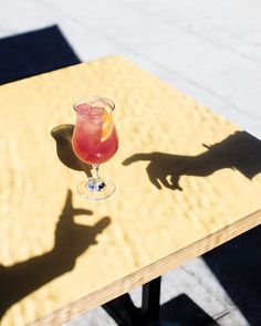 the shadow of a person's hand on a table with a drink in it