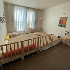 a bed sitting next to a window in a room with wooden floors and white walls