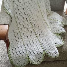 a white crocheted blanket sitting on top of a chair next to a pillow