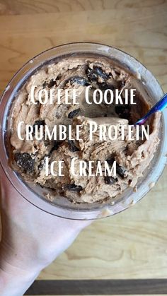 a hand holding a cup filled with coffee cookie crumble protein ice cream on top of a wooden table