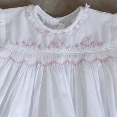 a white dress with pink flowers on the chest and collar, sitting on a wooden floor