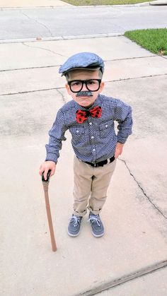 a young boy wearing glasses and a bow tie holding a cane in his hand while standing on the sidewalk