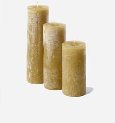 three pillar candles are lined up against a white background, one is yellow and the other is brown