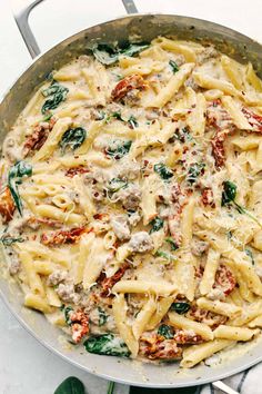 a skillet filled with pasta and spinach covered in sauce on top of a marble counter