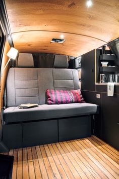 the interior of a camper van with wood flooring and gray couch, coffee maker on shelf