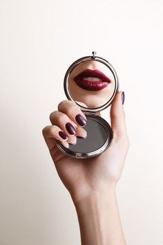 a woman's hand holding a compact mirror with a lipstick on it