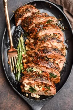 grilled pork chops and vegetables on a black plate with a gold fork next to it