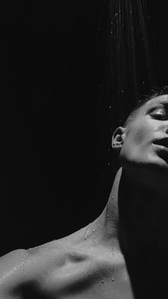 a black and white photo of a shirtless man with his head under the shower