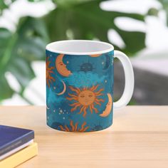 a coffee mug sitting on top of a wooden table next to a book and plant