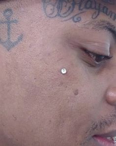 a close up of a person with a piercing on his nose and tattoos on his forehead