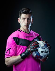 a young man in a pink shirt holding a soccer ball and gloves on his hands