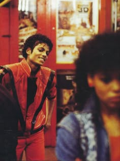 a man in red pants standing next to a woman with black hair and an orange jacket