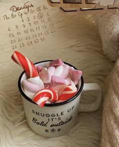 a mug filled with candy and marshmallows on top of a fur covered bed