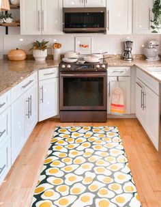 a kitchen with white cabinets and an area rug on the floor in front of the stove