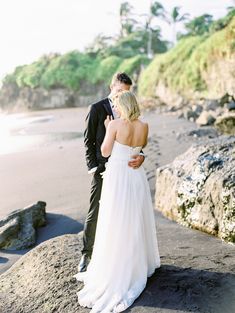 a bride and groom standing on the beach