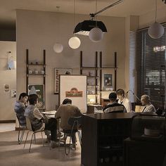 several people are sitting at a table in an office setting with hanging lights above them