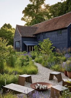 an outdoor seating area in front of a blue house with lots of plants and flowers around it