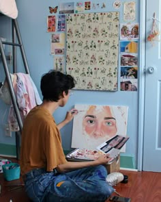 a young man sitting on the floor in front of an easel with his painting