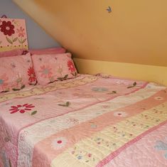 a bed with pink and yellow bedspread next to a slanted wall in a bedroom