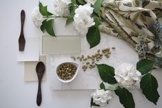 white flowers and green leaves on a table next to spoons, napkins and utensils