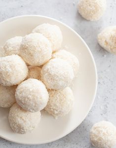 a white plate filled with coconut snowballs on top of a marble countertop next to small pieces of fruit