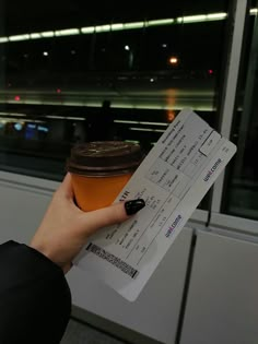 a person holding up a receipt and a cup of coffee in front of a window