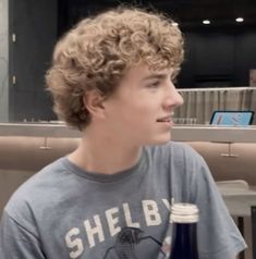 a young man sitting at a table with a bottle of beer in front of him