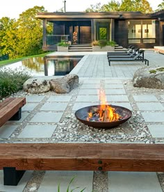 a fire pit sitting on top of a wooden bench next to a swimming pool in front of a house