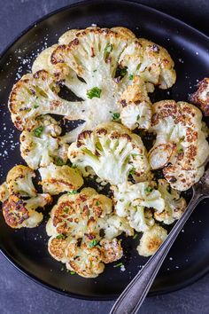 cauliflower florets on a black plate with a silver spoon and sprinkled parmesan cheese