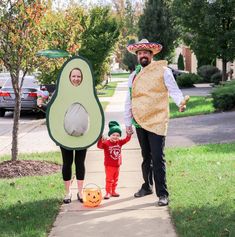 a man and woman in costumes standing next to a child holding an avocado