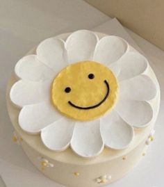 a white cake with a yellow smiley face on it's frosting and flower decoration