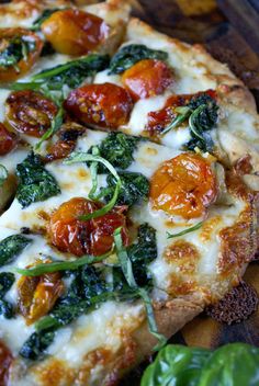 a pizza with tomatoes, spinach and cheese on it sitting on a cutting board