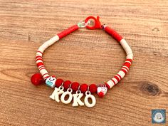 a red and white beaded bracelet with the word toko on it, sitting on top of a wooden table