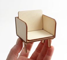 a hand holding a miniature chair made out of plywood and paper with the seat folded down