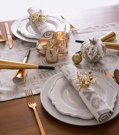 a table set for christmas with gold and white decorations on it, silverware and napkins