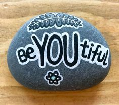 a rock with the words be you tiful painted on it sitting on a wooden surface