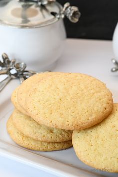 three cookies on a white plate next to a tea pot