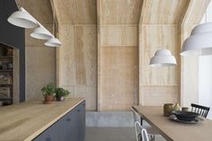 an empty kitchen and dining room with wood paneling on the walls, along with white pendant lights