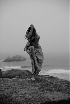 a woman standing on top of a rock next to the ocean with her arms in the air