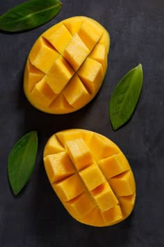 two pieces of mango sitting on top of a black surface next to green leafy leaves