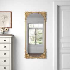 an ornate gold framed mirror hangs on the wall next to a white chest of drawers