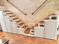 the stairs are built into the wooden wall in this room with white cabinets and drawers