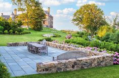 a stone patio surrounded by flowers and greenery in front of a castle like building